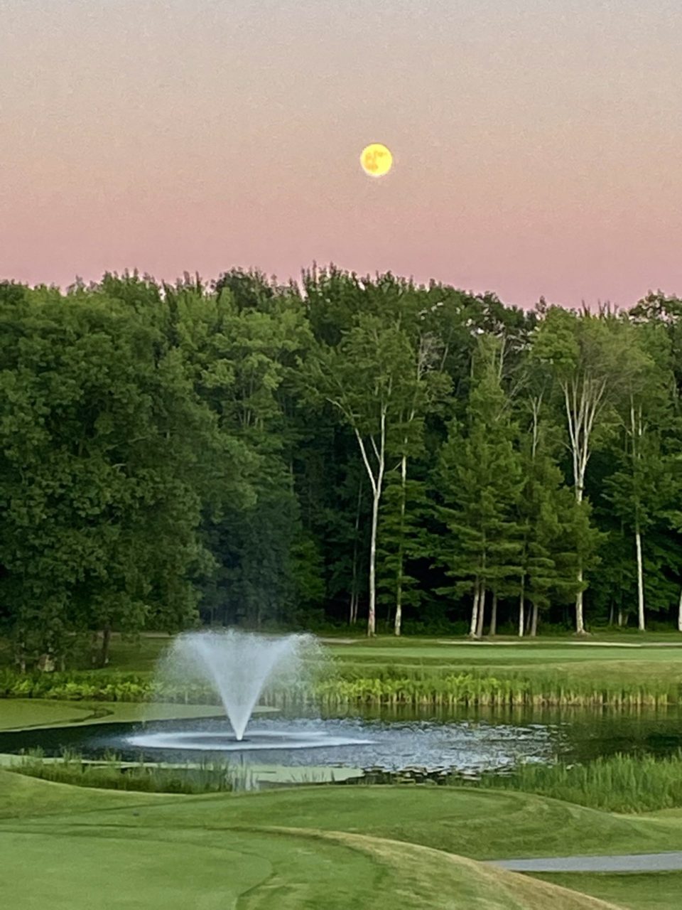 Water fountain on a golf course with full moon in background